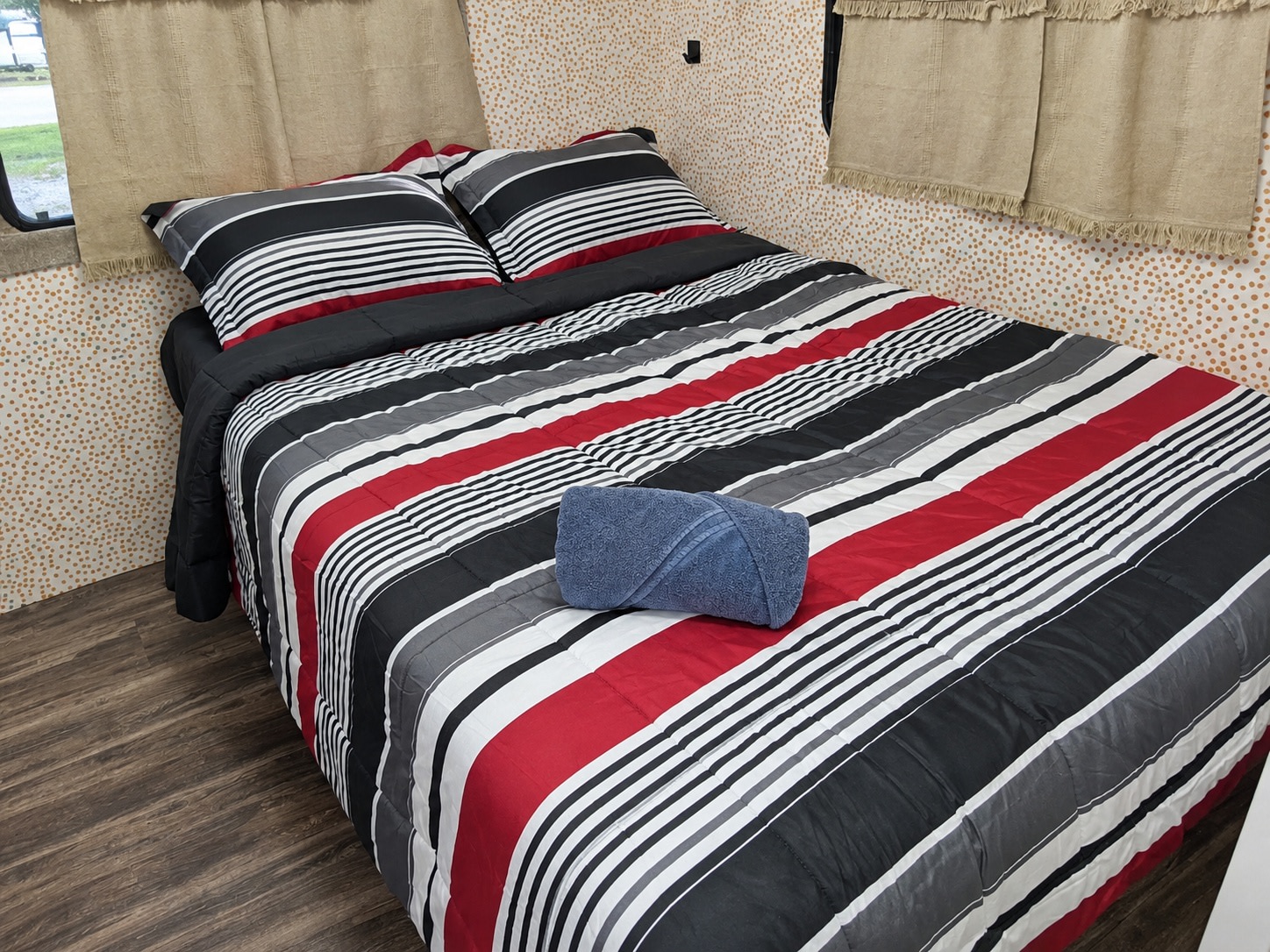 Inside an rv rental: a cozy bedroom with red, black, and white striped bedding, a blue towel, and wood-look flooring.. Coachman Mirada 2011