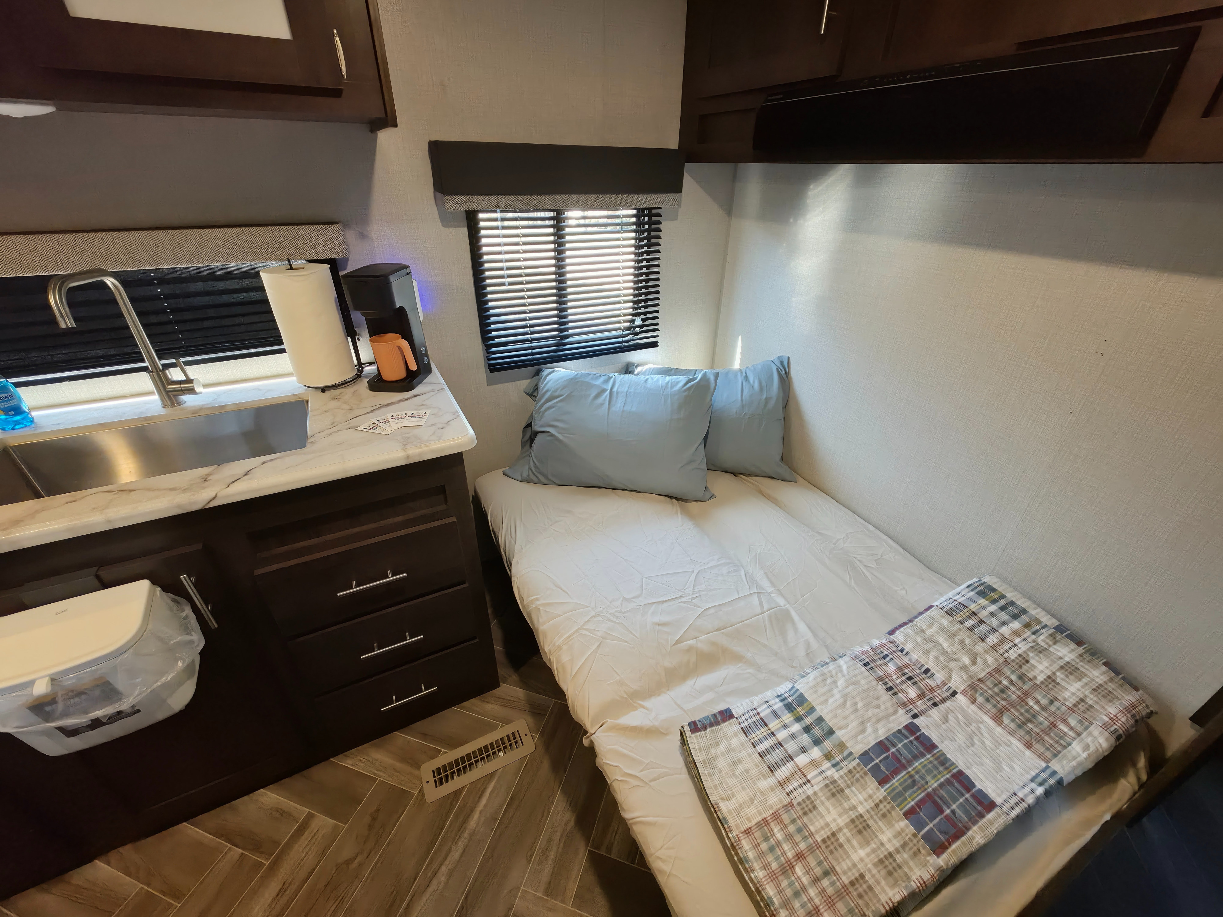Cozy rv rental interior: compact kitchen area with sink, and a comfortable bed with light blue pillows & plaid quilt.. KZ Sportsmen SE 260BHSE 2020