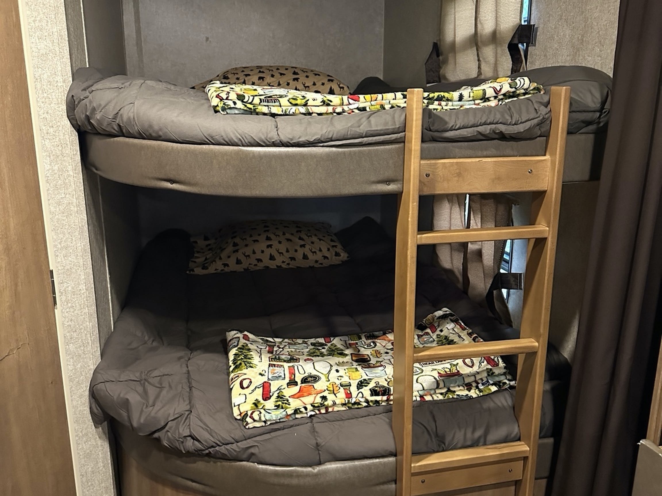Two cozy bunk beds in an RV rental, featuring grey bedding, patterned pillows & blankets, and a wooden ladder for access.. Coachmen Catalina 2017