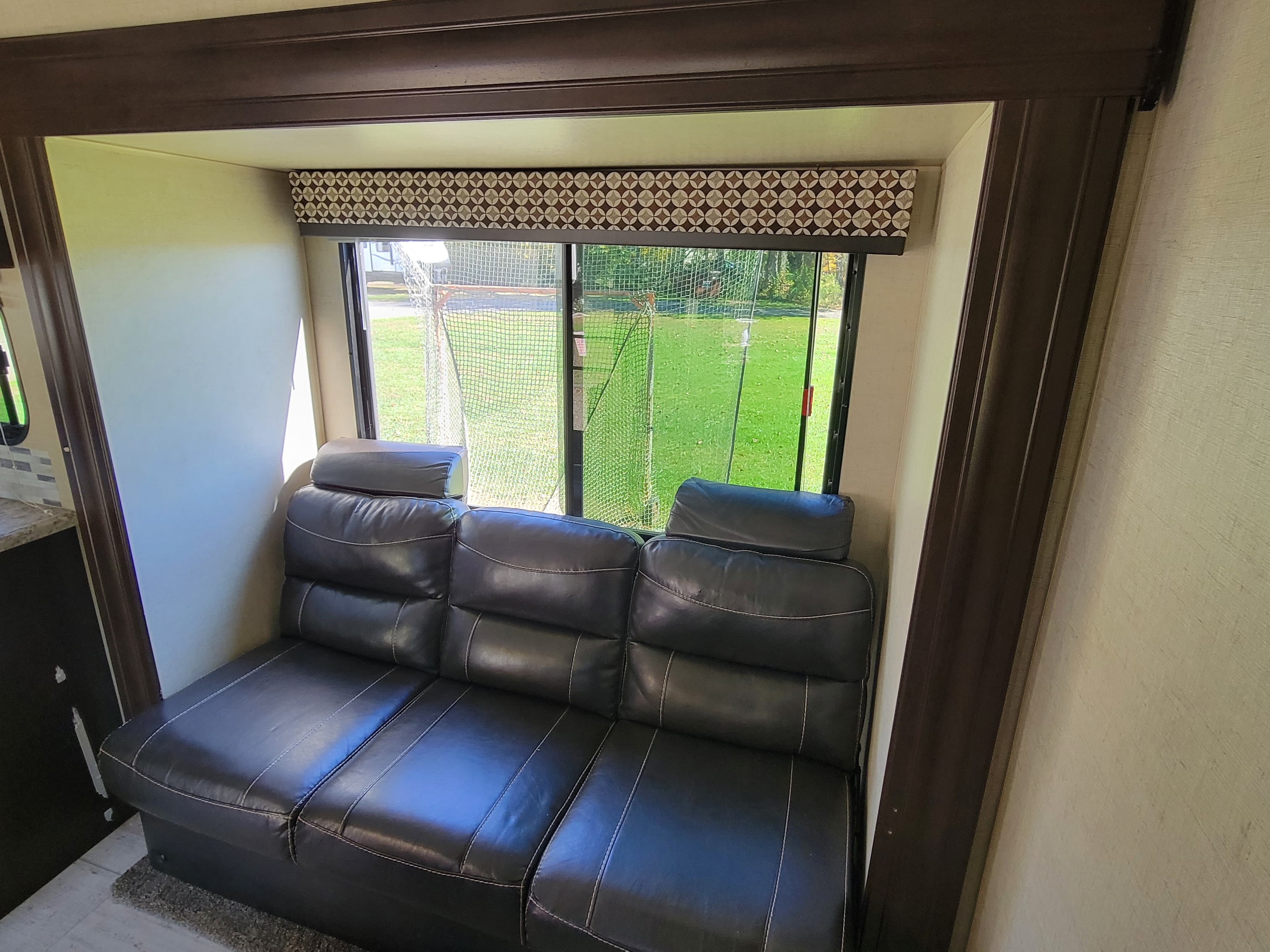 Inside an RV rental: a plush black leather sofa in a cozy living area with a window view to green outdoors.. KZ 231RKLE 2018