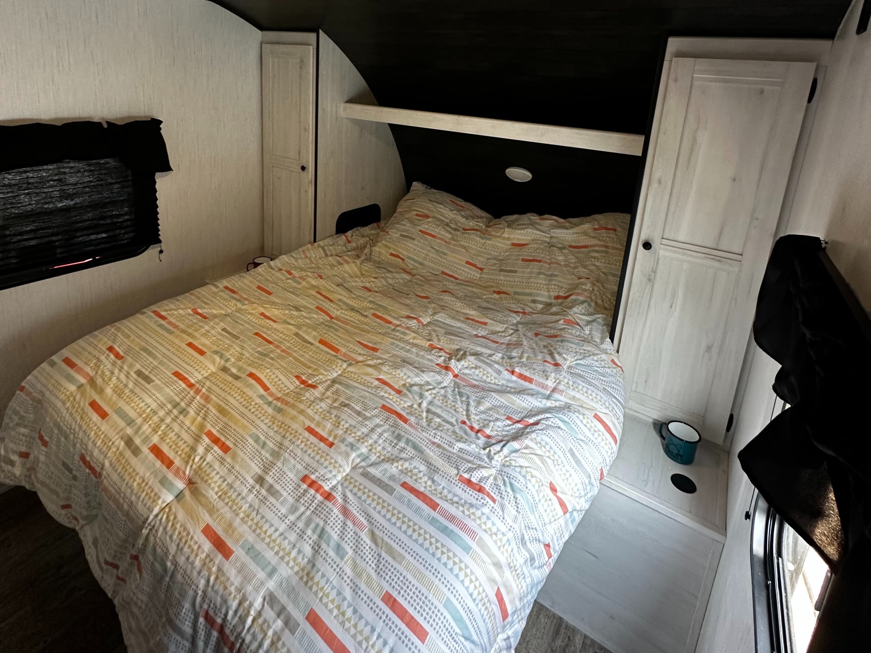 Cozy RV rental bedroom with a patterned comforter, built-in storage, and window, providing a comfortable sleeping area.. Heartland Trail Runner 2022