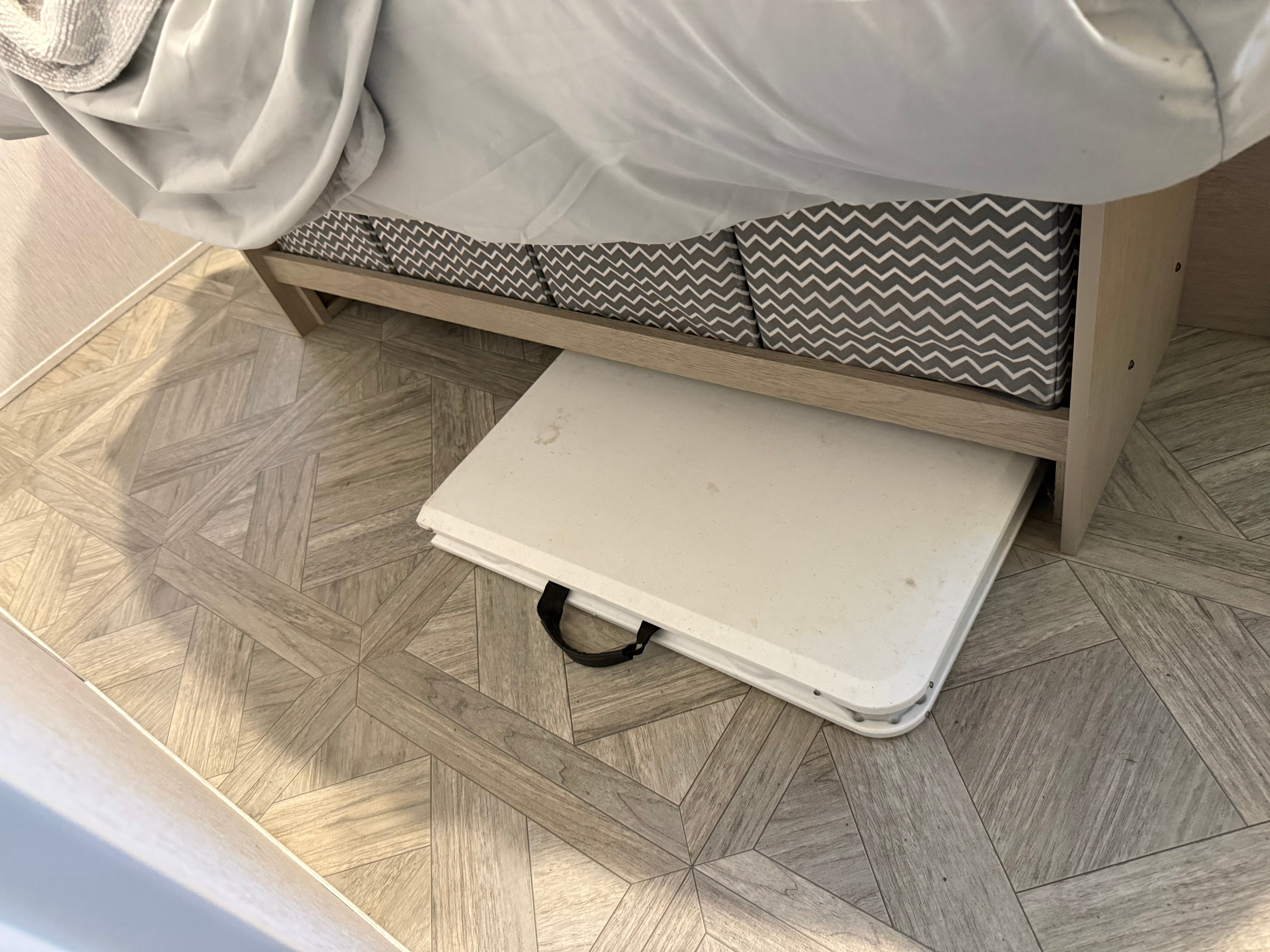 Smart storage for your RV rental: A folded portable table is neatly tucked under the bed, alongside chevron bins.. Forest River Wildwood X-Lite Platinum 2024