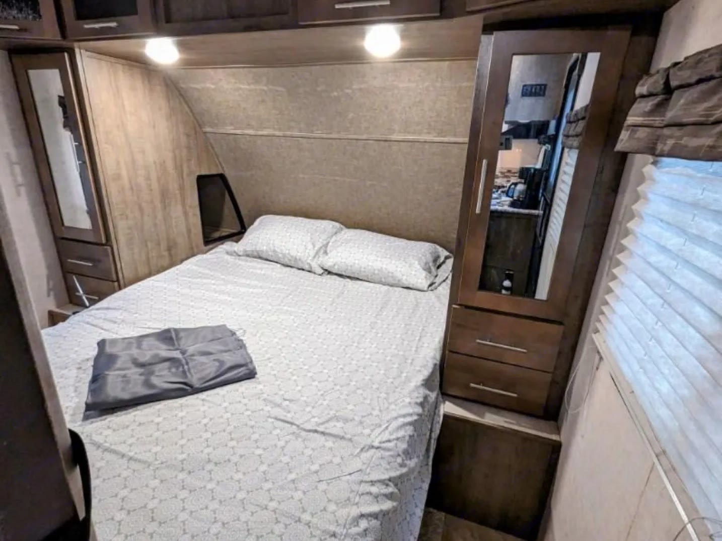 This RV rental's cozy bedroom features a comfortable double bed with light sheets, overhead cabinets, and mirrored wardrobes.. Forest River Surveyor 2017