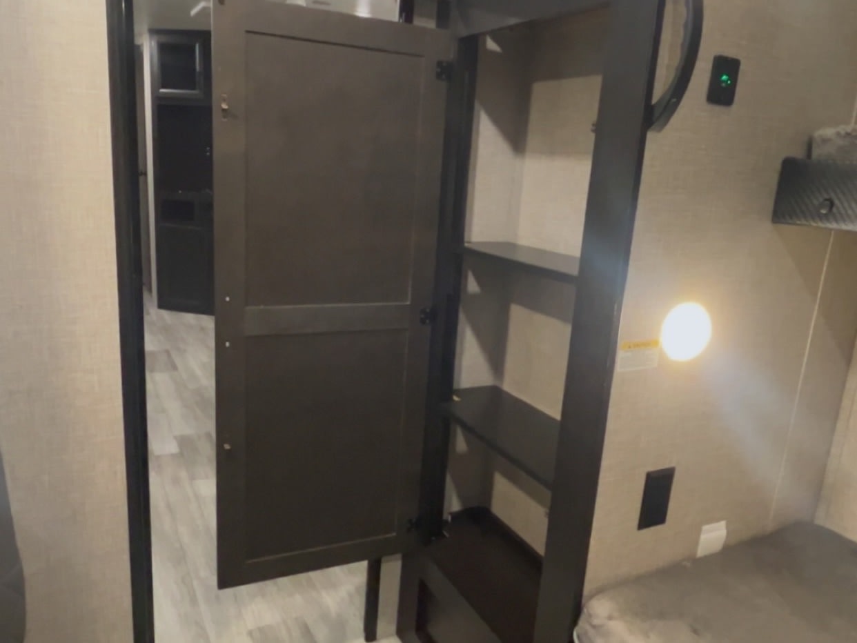 RV rental interior: Open storage cabinet with shelves by a bunk, modern lighting, outlets, and a hallway view.. Jayco Jay Flight 2023