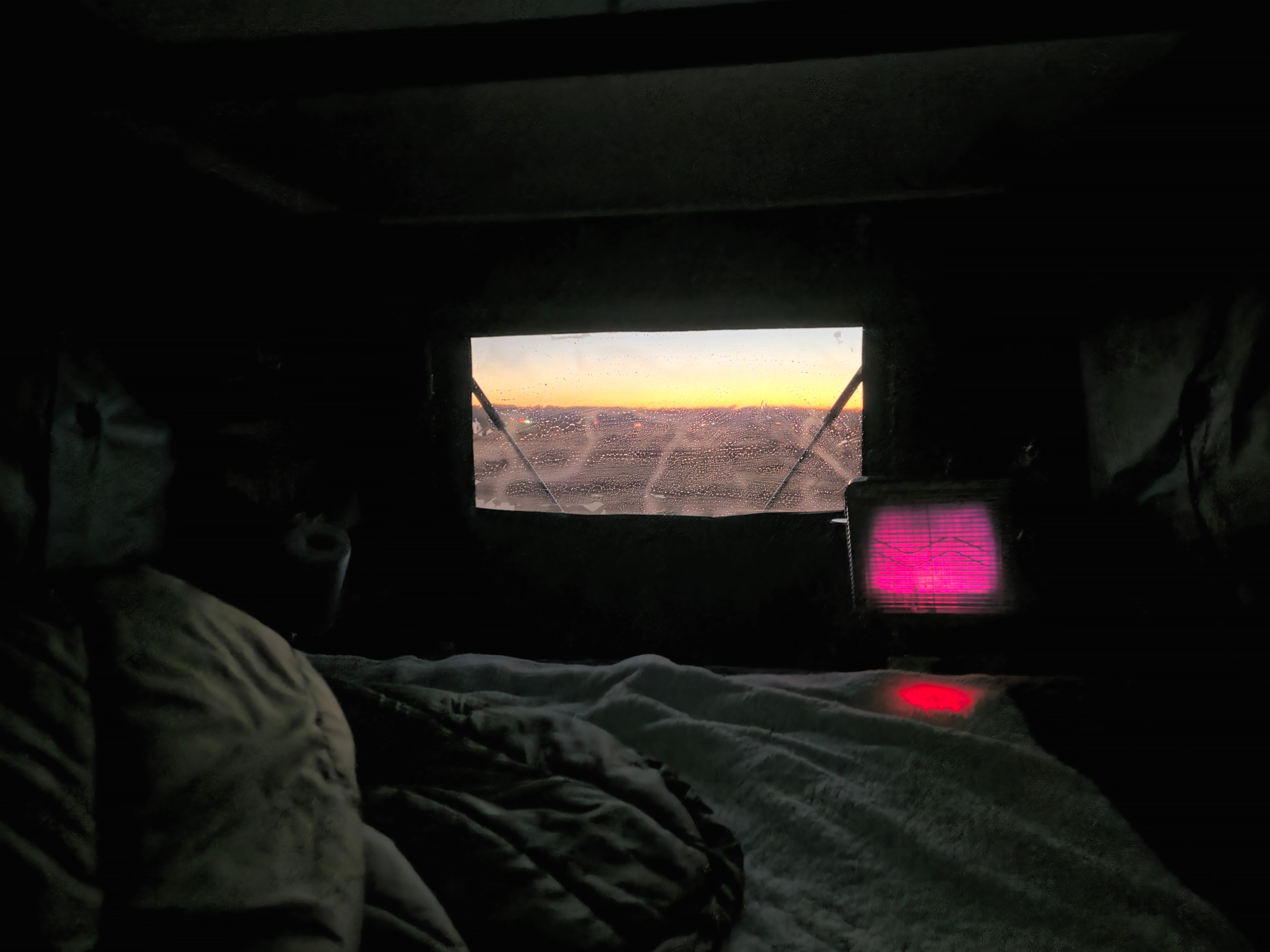 Cozy RV rental interior with a warm bed, glowing heater, and condensation-covered window showing a vibrant sunrise.. Jeep Gladiator 2020