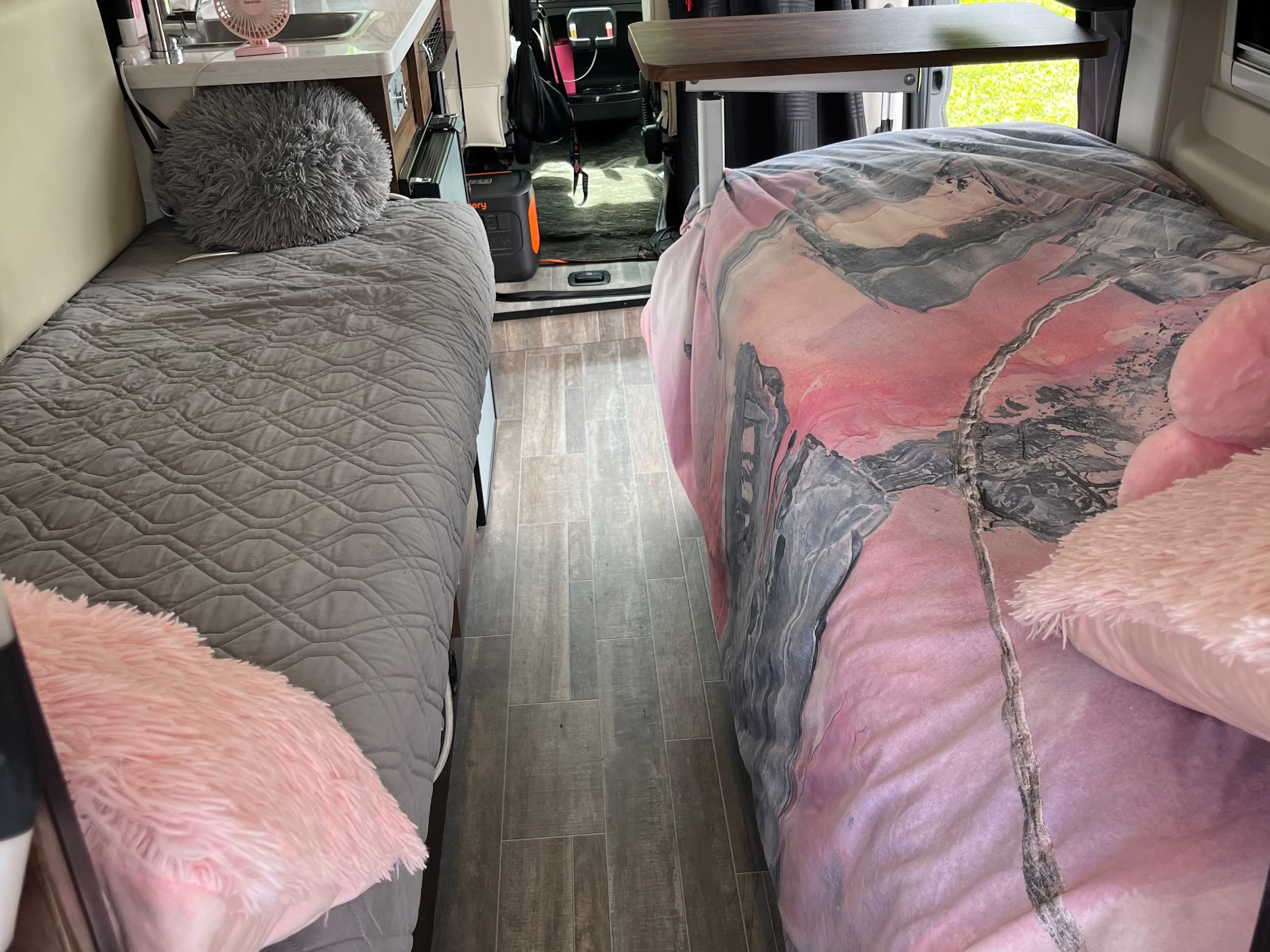Inside a cozy RV rental: two beds with stylish bedding, a central aisle, and a table. Ready for adventure.. Winnebago Travato 2024