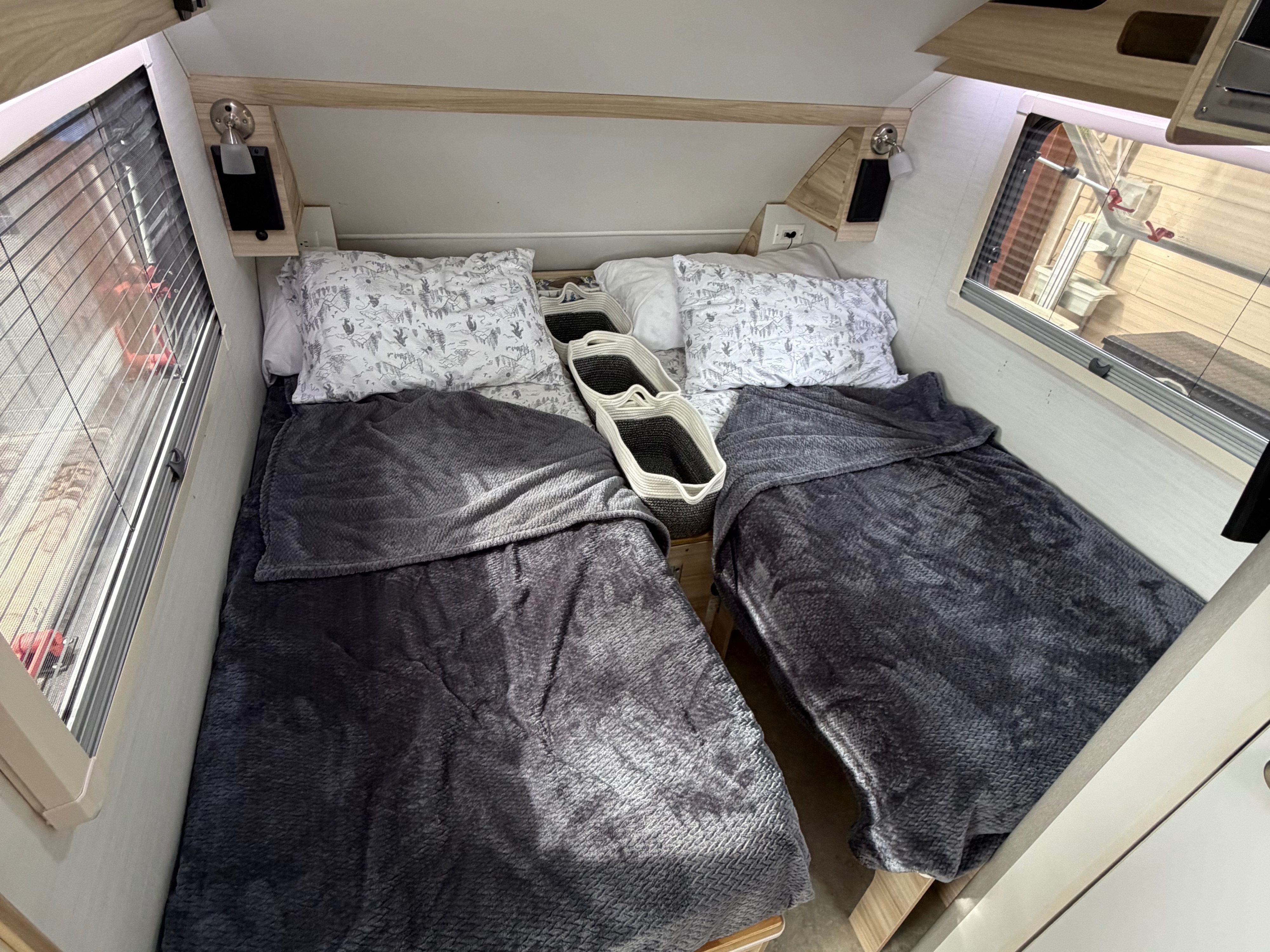 Inside an RV rental: two comfy beds with grey blankets, pillows, and baskets for storage, perfect for a cozy camping trip.. nuCamp T@B 2024