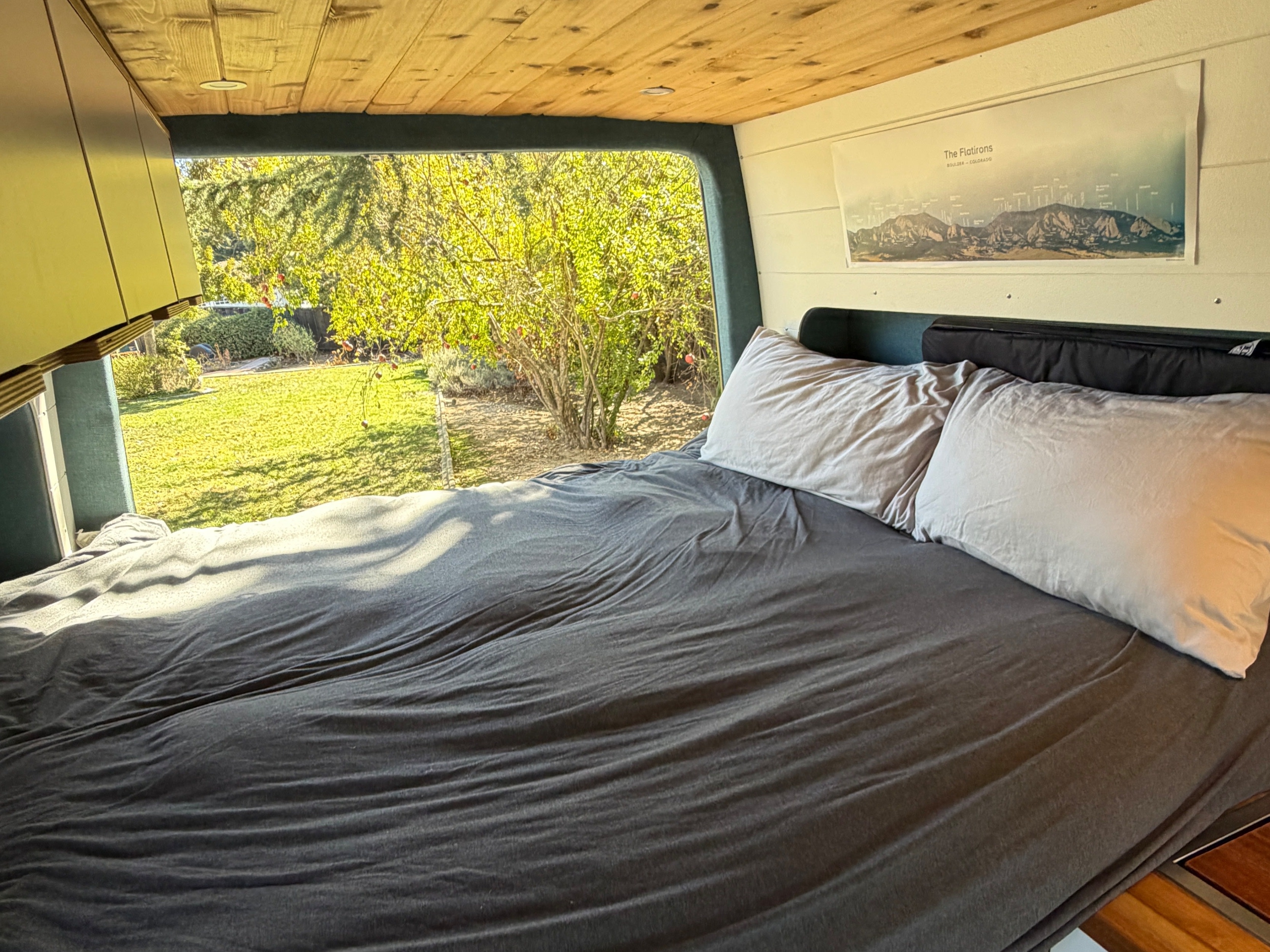 Experience cozy van life in this RV rental's inviting bedroom. Features a comfy bed, wood ceiling, and scenic garden view.. Mercedes-Benz Sprinter 2019