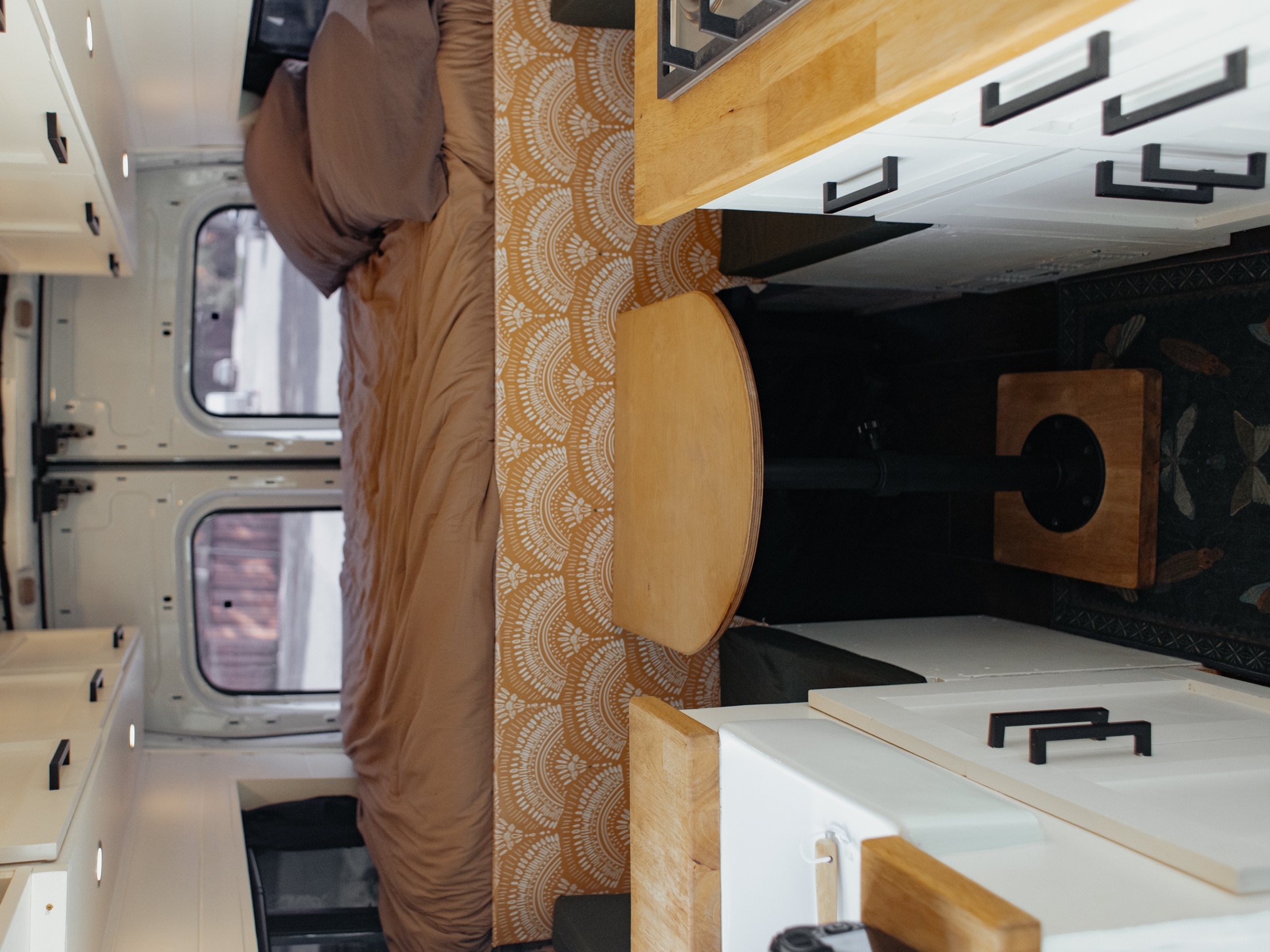 Cozy RV rental interior featuring a compact kitchen, comfortable bed, and dining table, perfect for van life adventures.. Ford Transit 2015