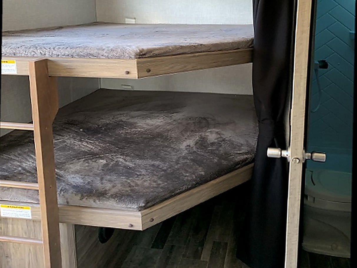Cozy RV rental bunk beds with dark, plush mattresses and a ladder, offering compact sleeping space and a nearby bathroom.. Crossroads RV Zinger Lite 2021