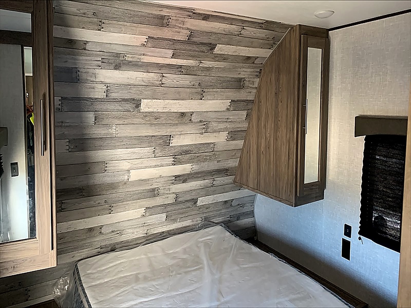 RV rental bedroom featuring a distressed wood-plank accent wall, plastic-wrapped mattress, and overhead storage cabinet.. Crossroads RV Zinger Lite 2021