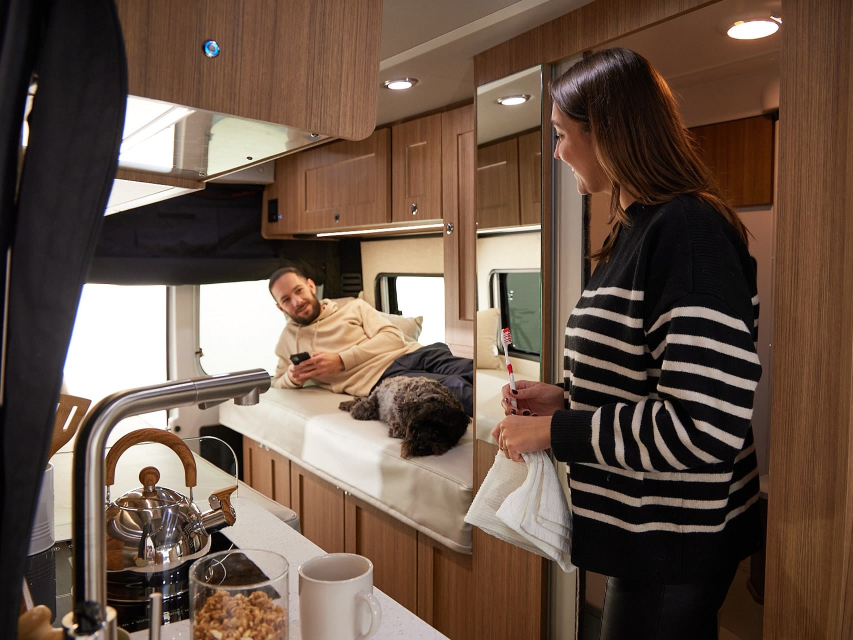 Enjoying an RV rental: a woman doing her morning routine while a man and their dog relax in their cozy camper.. Roadtrek PIVOT SLUMBER 2024