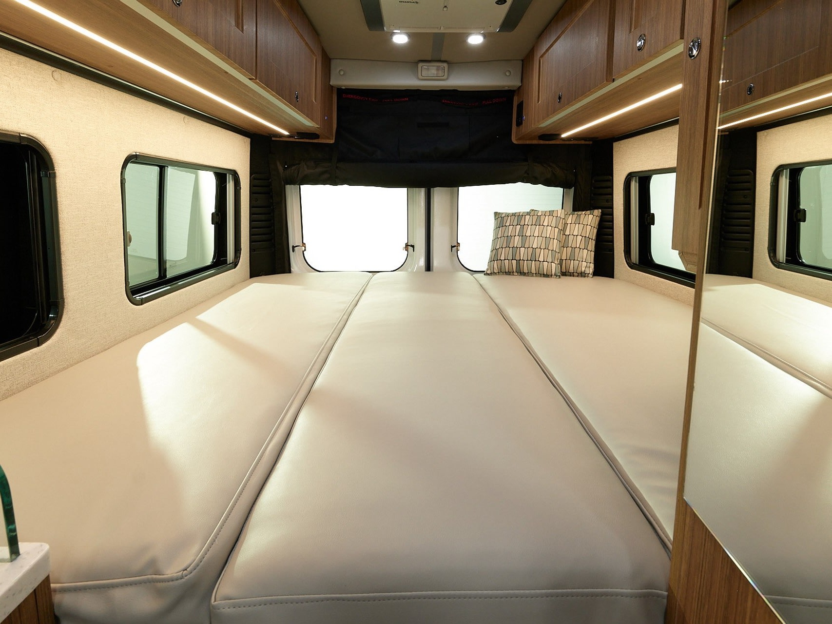 This inviting rv rental interior showcases a cozy, light-toned bed setup, complete with side windows and ample storage.. Roadtrek PIVOT SLUMBER 2024