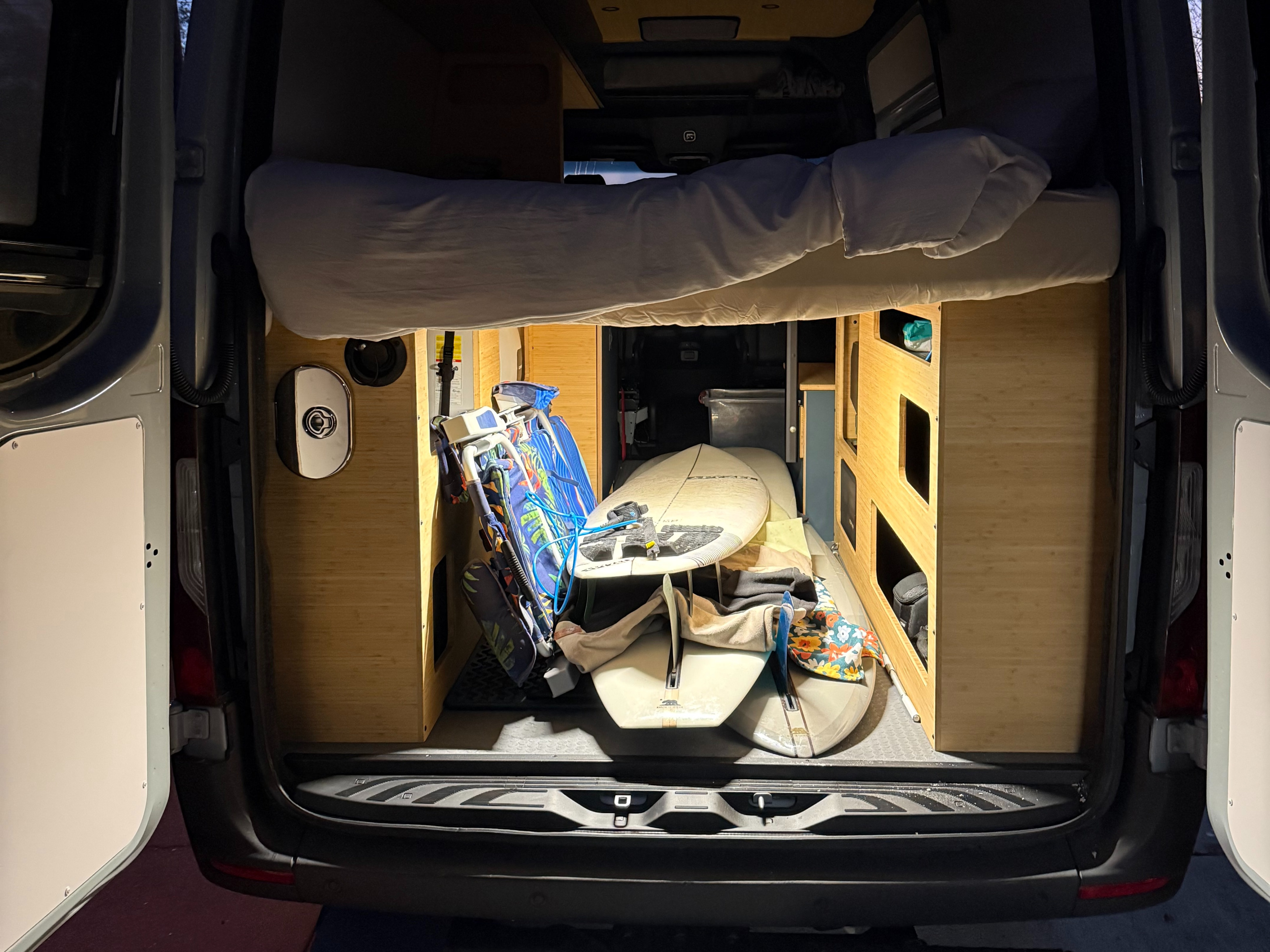 Inside an RV rental van: rear view showing a comfy raised bed, ample storage for surfboards and adventure gear.. Mercedes-Benz Sprinter 2026