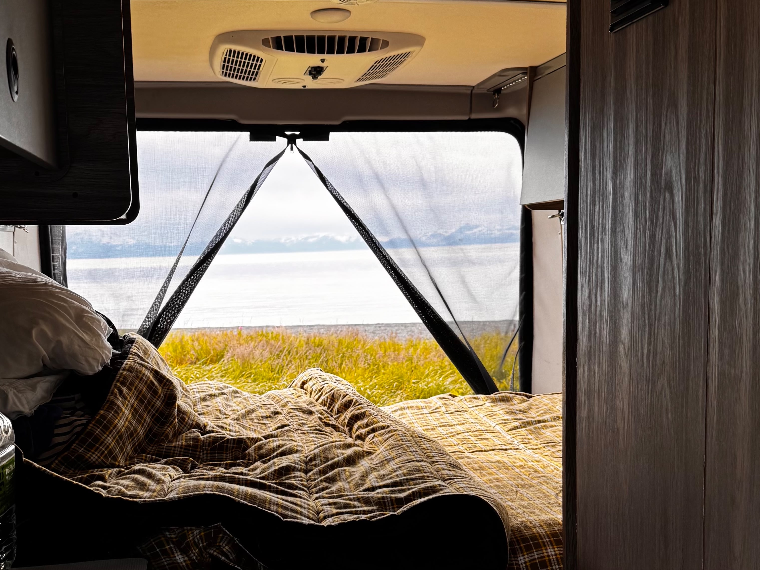 Cozy RV rental bed with an ocean view through the mesh screen. Perfect for a scenic campervan travel experience.. Winnebago Solis 59PX 2025