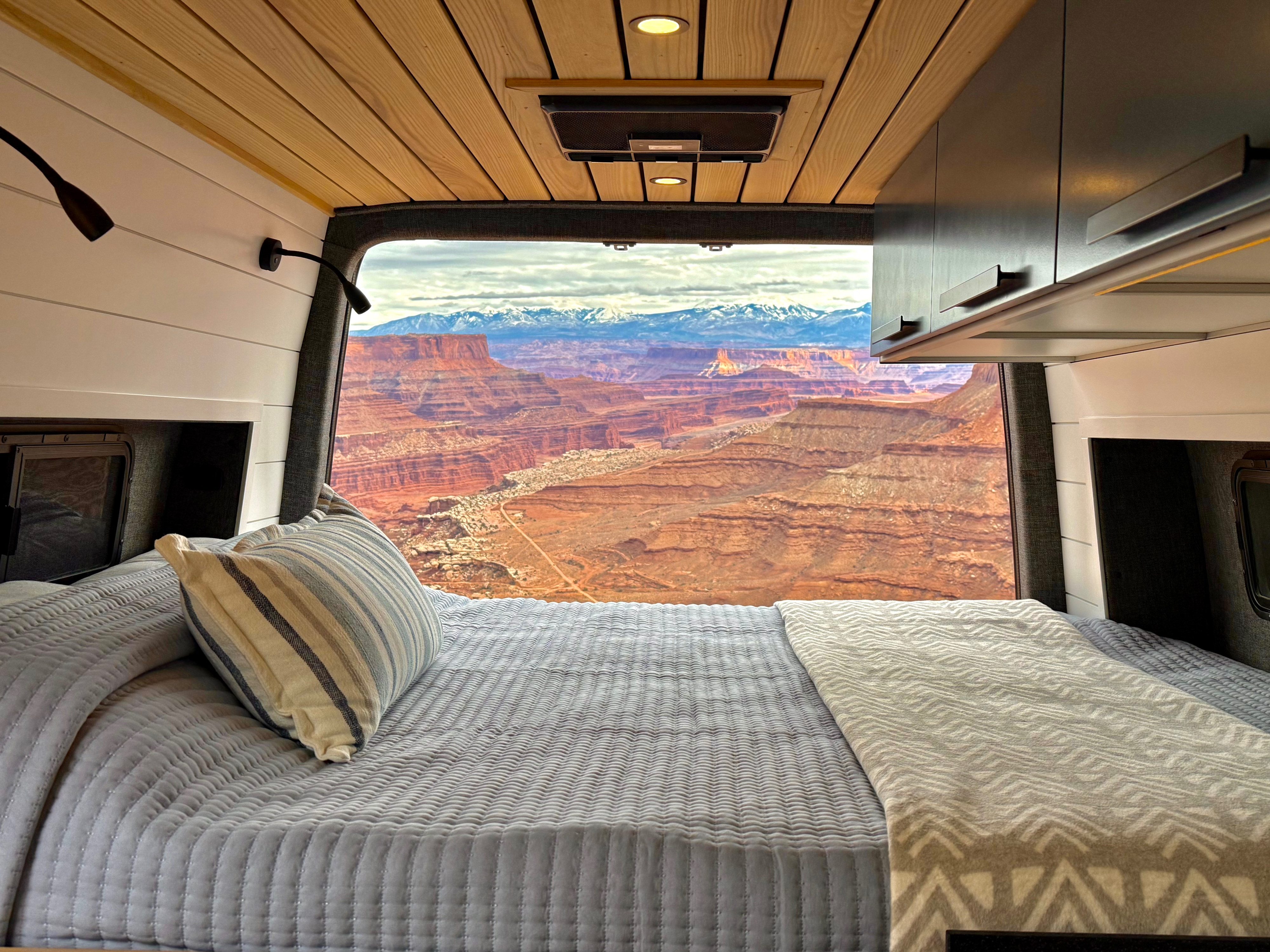 Cozy rv rental bed with a stunning view of red rock canyons and distant snow-capped mountains.. Mercedes-Benz Sprinter 2023