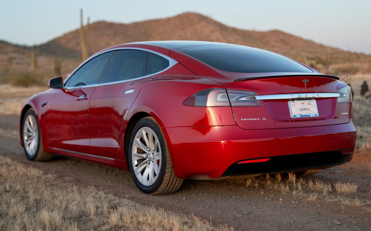 A sleek red Tesla Model S on a dirt road, offering a different adventure than an RV rental in the desert