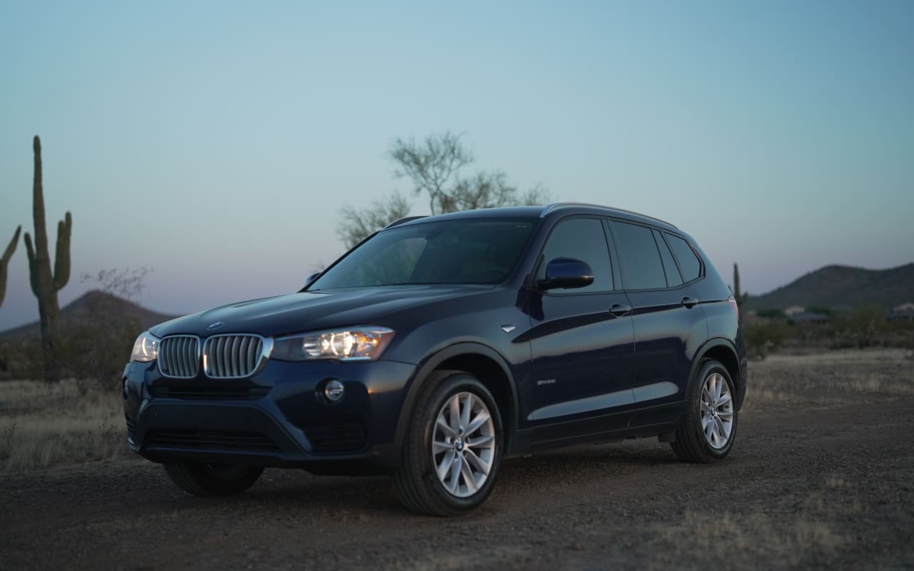A dark blue SUV in a desert landscape with saguaro cacti at dusk