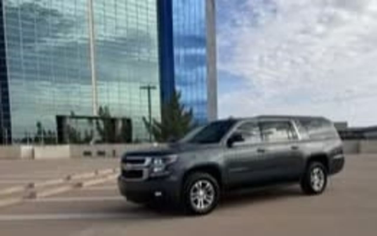 A dark gray Chevrolet Suburban SUV parked by a modern glass building