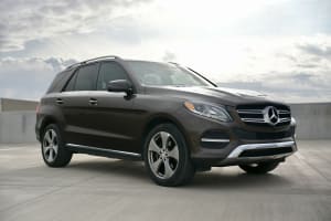 A sleek brown Mercedes-Benz SUV, perfect for car rental, sits on a concrete deck under a cloudy sky