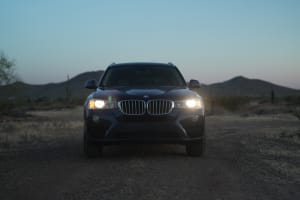 Dark SUV with bright headlights on a desert dirt road at dusk, mountains behind