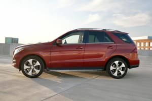 A red Mercedes-Benz GLE SUV, suitable for car rental, parked on a sunny rooftop under a bright sky