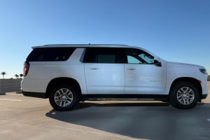 A large white SUV, like a Suburban, gleaming under a blue sky on a parking deck
