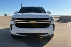 Front view of a large white Chevrolet Suburban SUV, ideal for car rental, parked under a clear sky
