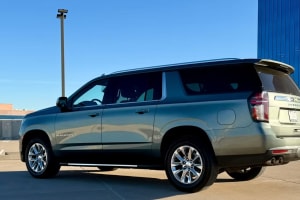 A sleek, dark green Chevrolet Suburban SUV is parked outdoors on a sunny day