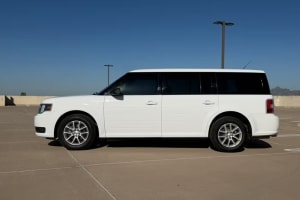 Side view of a white Ford Flex car rental parked in an empty concrete lot under a clear blue sky, ideal for travel