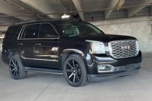Sleek black GMC Yukon Denali SUV, a spacious car rental option, parked in a concrete garage