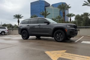 Dark gray Jeep Grand Cherokee SUV in an urban setting with palm trees & modern buildings