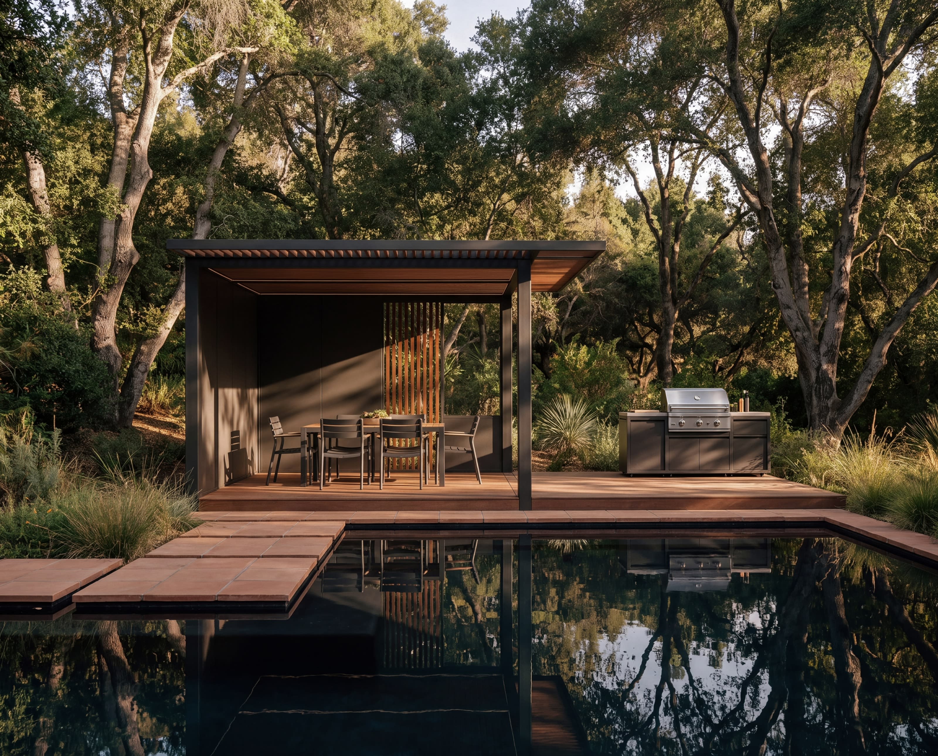 An OS1 dining pavilion and outdoor grill on a timber deck beside a pool in a wooded garden
