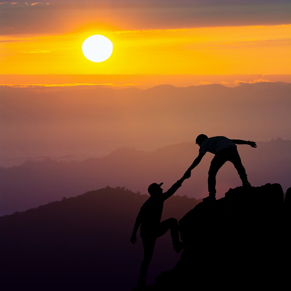 Teamwork of two men hiker helping each other on top of mountain climbing team beautiful sunrise landscape