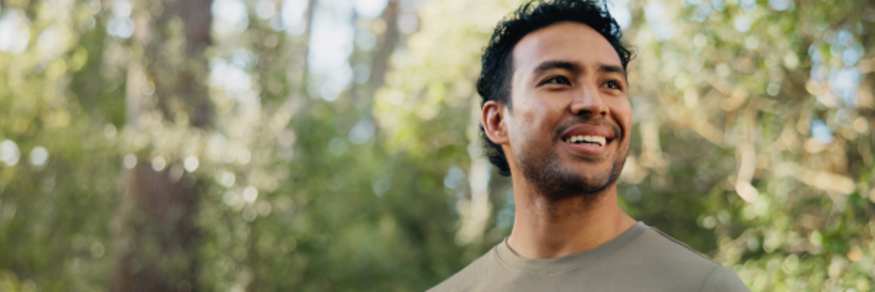 man with black hair smiling in nature with green t-shirt