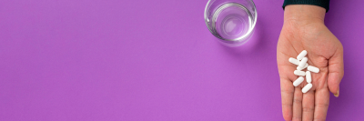 woman's hand holding tablets on a purple background with a glass of water