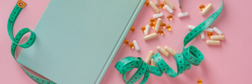 tablets, capsules, measuring tape and book on pink background