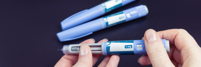 Two weight loss injections on the table and one held in a person's hand