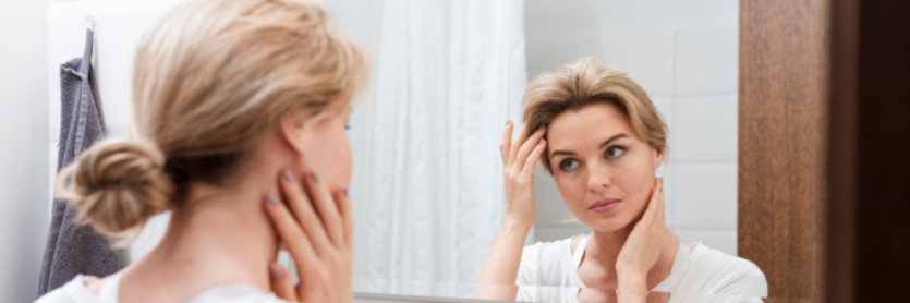 Blond woman looking touching face in the mirror