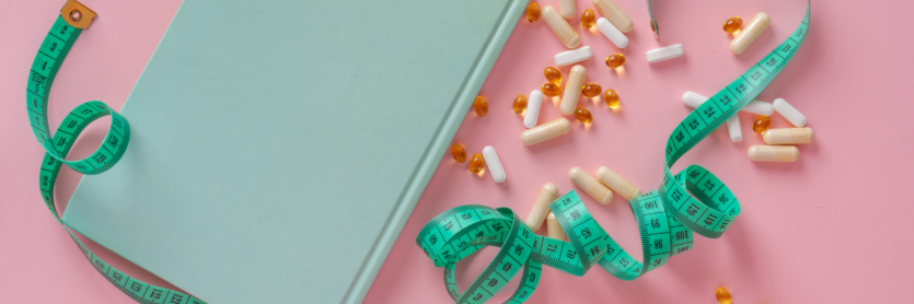 tablets, capsules, measuring tape and book on pink background
