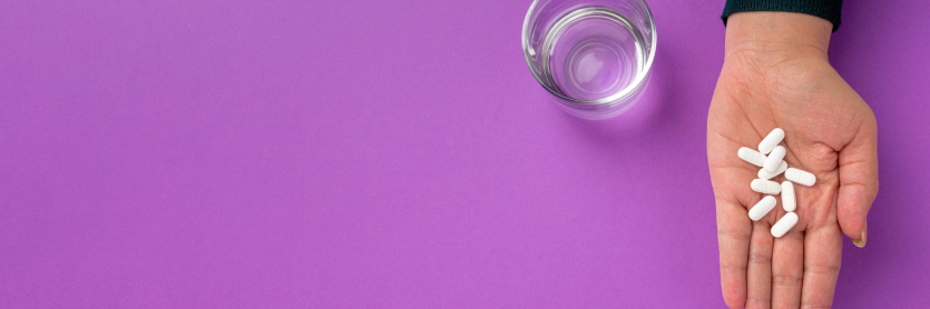 woman's hand holding tablets on a purple background with a glass of water