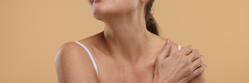 older woman touching her shoulder in white vest top