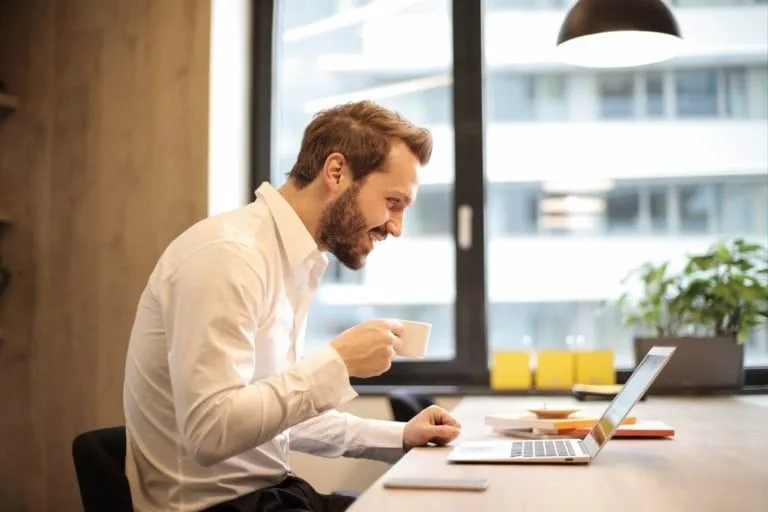 man-holding-teacup-infront-of-laptop-on-top-of-table