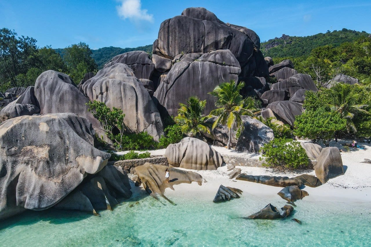 Image taken by Michelle Chu at Anse Source D'Argent, with a woman standing in the centre on the beach and granite boulders around and behind her.