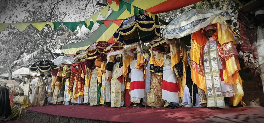 Orthodoxe Priester in bestickten Gewändern mit zeremoniellen Schirmen feiern Timkat