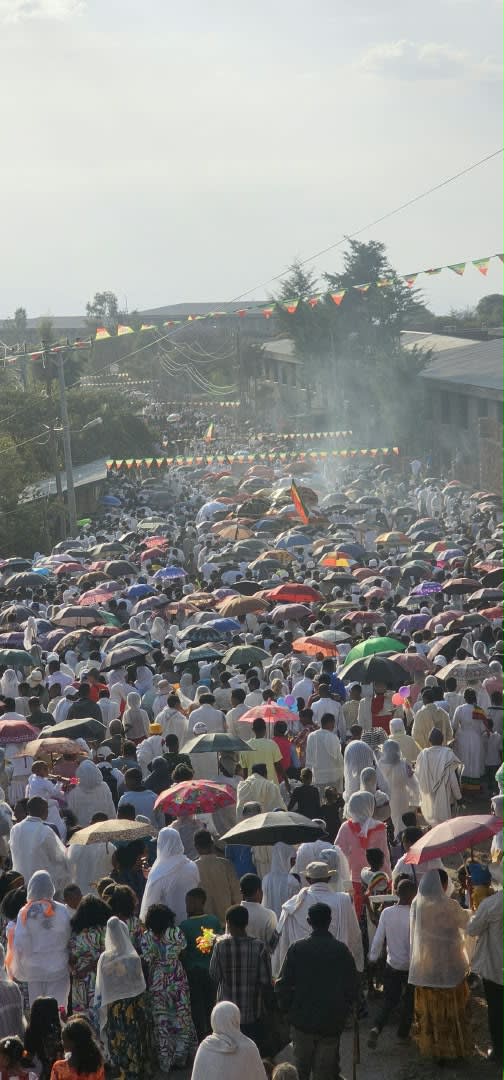 Une foule munie de parapluies et de drapeaux remplit la rue lors d’une procession festive
