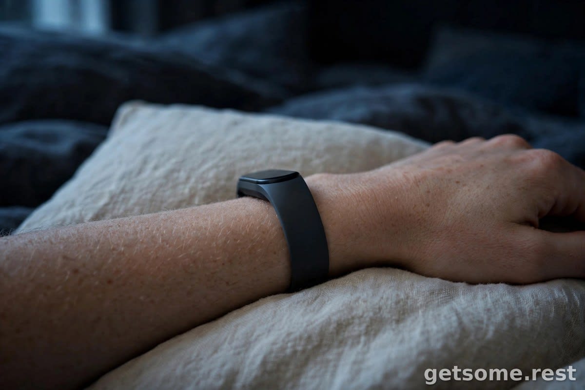 Close-up of a slim fitness tracker band on a wrist resting on a pillow at night