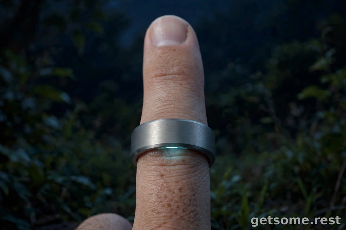 Close-up of a titanium smart ring on a finger at night with a faint sensor glow