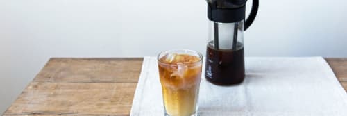 An iced coffee and half full coffee pot on a table