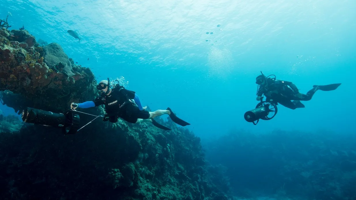Two divers using a diver propulsion vehicle underwater.